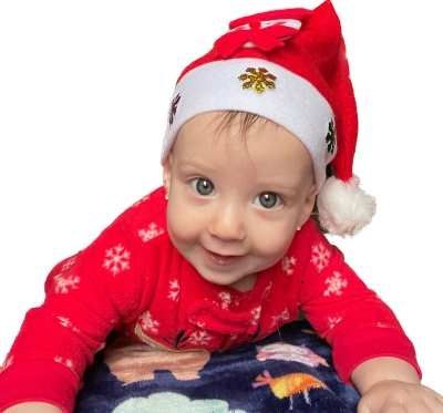 Baby wearing a Santa hat and red onesie with snowflake design, smiling.