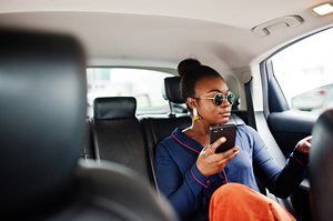 Woman in a car looking at a smartphone, wearing sunglasses and bright orange pants.