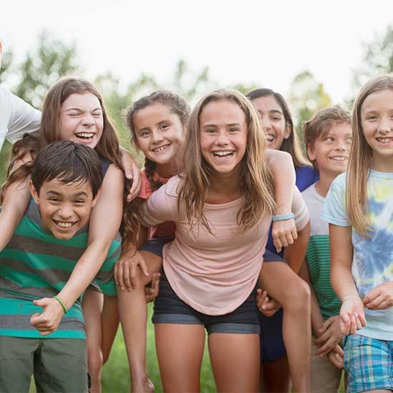 Group of children smiling and laughing outdoors, some giving piggyback rides.