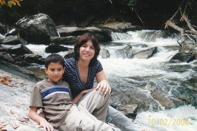 Woman and child sitting by a rushing stream, date stamp 10/02/2004, trees and rocks in background.