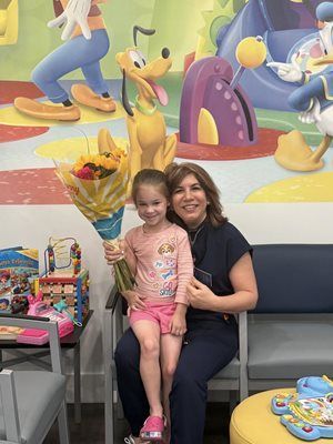 Woman and child with flowers, smiling, sitting in front of a Disney mural.