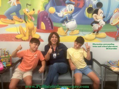 Two boys and a woman smiling, sitting in front of a Disney mural, giving thumbs up.