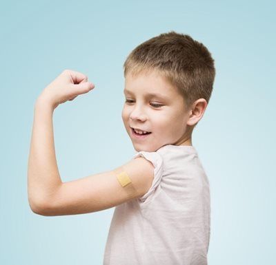 Boy smiles, flexing arm with adhesive bandage.