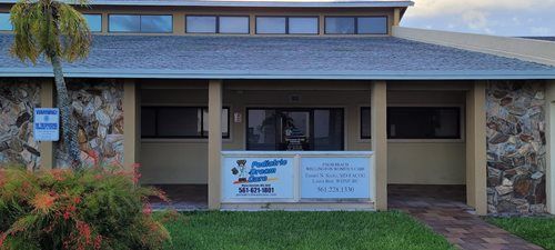 Building entrance with signage for a council and secretary. Stone and beige exterior, with windows and landscaping.