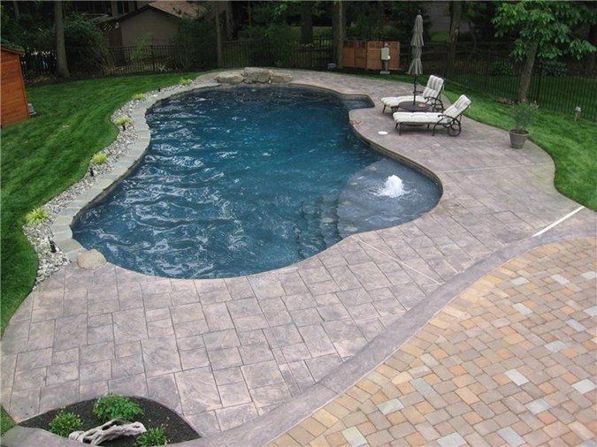 A large swimming pool surrounded by lawn chairs and a brick patio