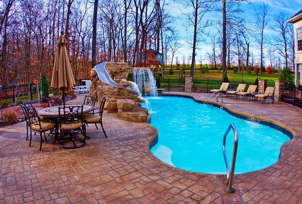 Swimming pool with a rock waterfall, slide, and patio furniture.