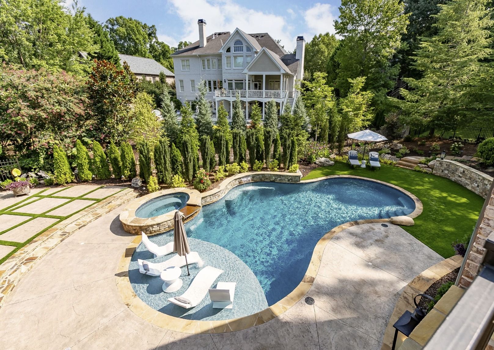 Luxury home with pool, spa, and landscaping; blue water, white lounge chairs.