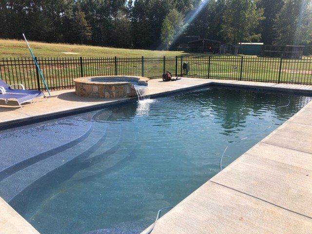 A large swimming pool with a hot tub and a fence around it.