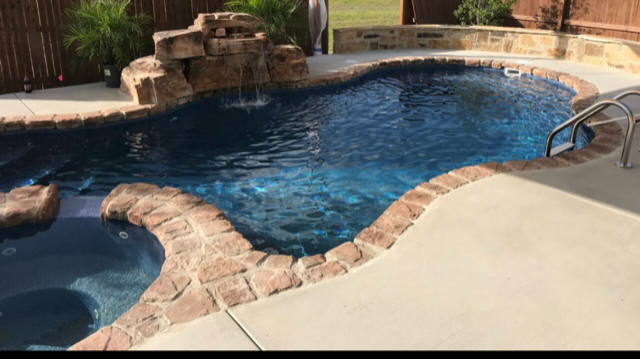 A large swimming pool with a waterfall in the backyard.