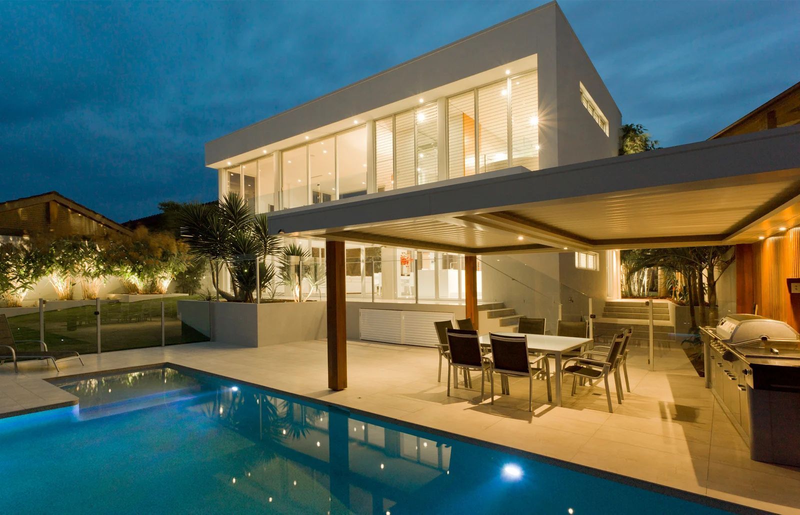 Modern home exterior with pool and patio at dusk.