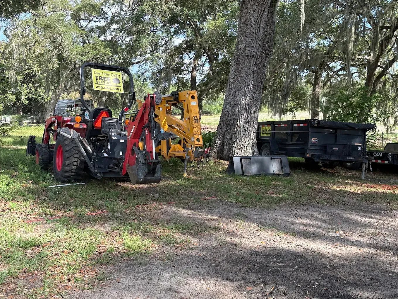 Red tractor with front loader parked beside a black trailer under trees in a grassy yard.