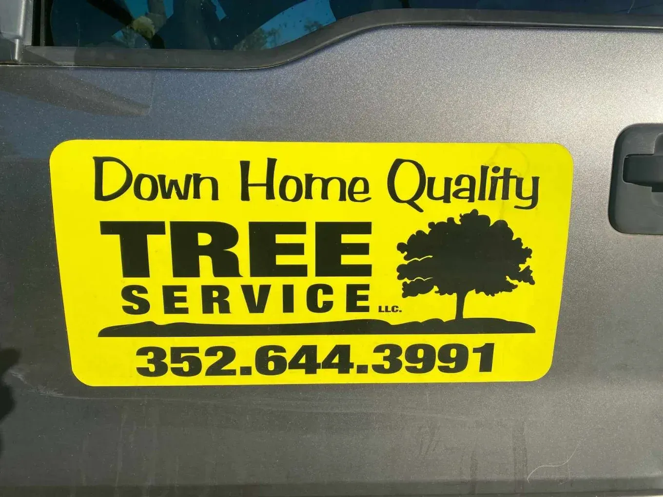 Yellow “Down Home Quality Tree Service” sign with phone number 352-644-3991 and tree silhouette.