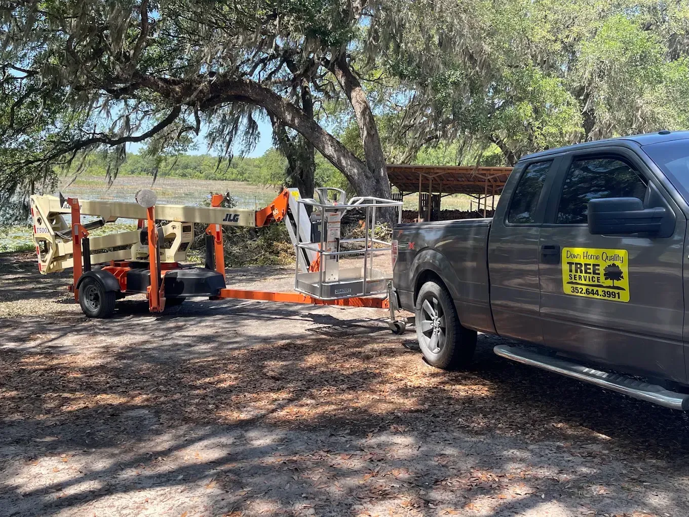 Gray pickup truck towing an orange trailer under trees on a dirt road
