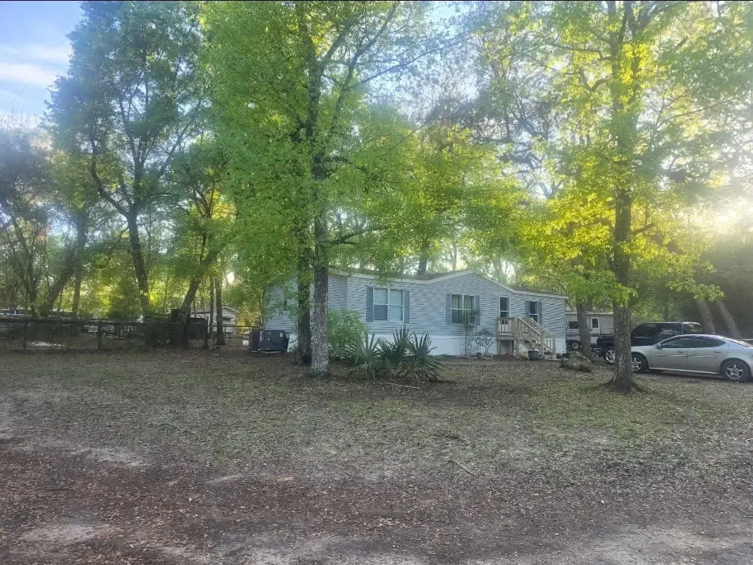 Small house under leafy trees with a parked car in a wooded yard