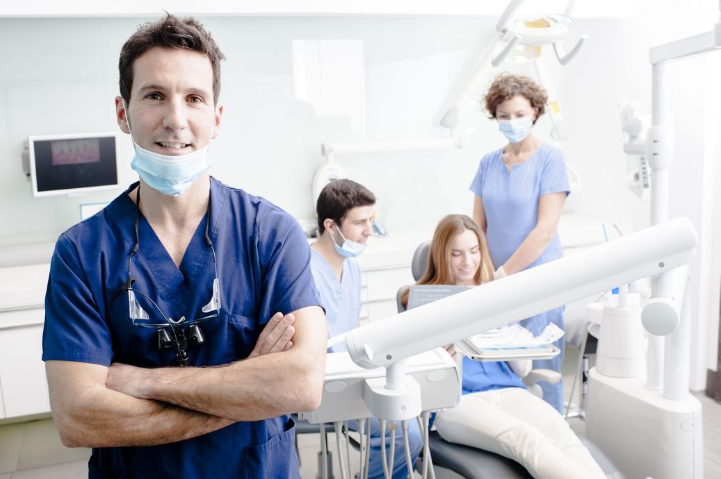 A dentist is standing in a dental office with his arms crossed.