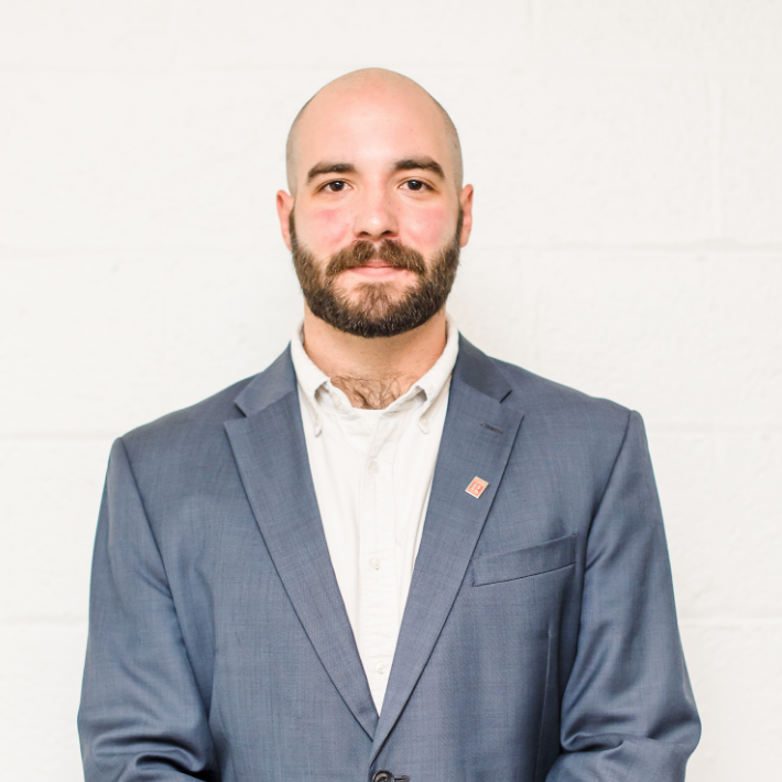 A bald man with a beard is wearing a blue suit