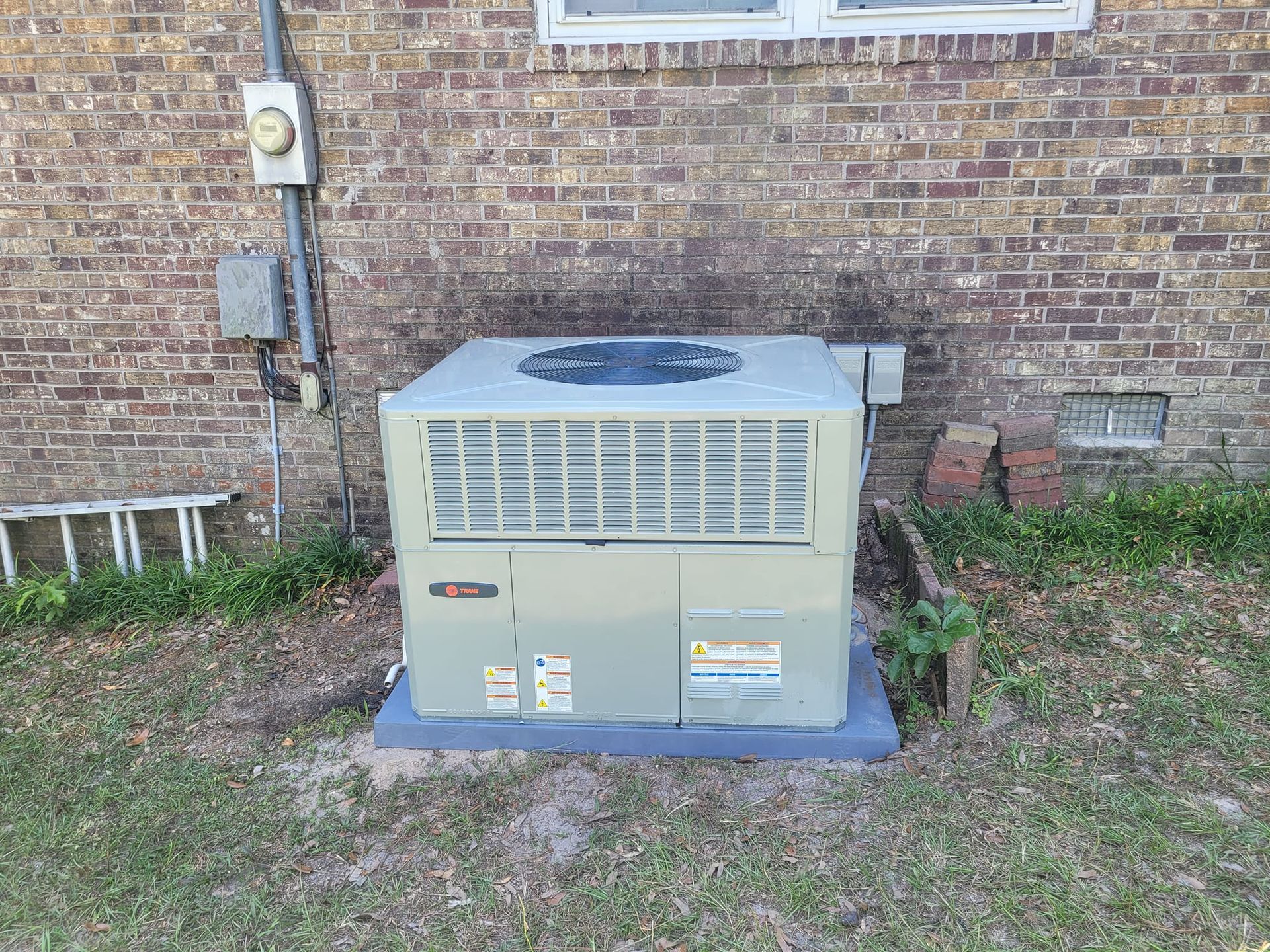A large air conditioner is sitting on the side of a brick building.