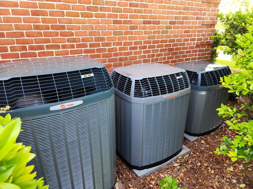 Three air conditioners are sitting outside of a brick building.