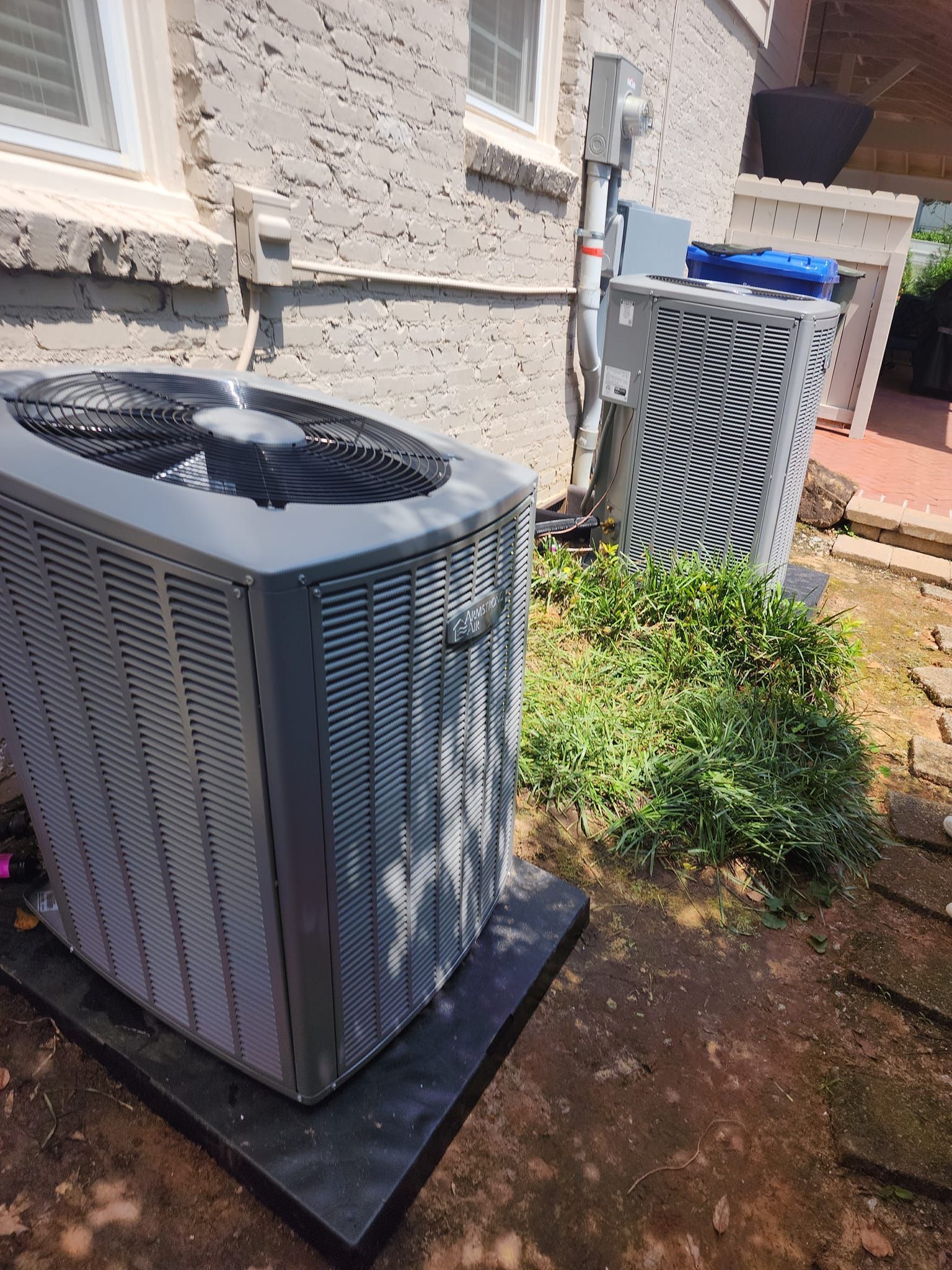 Two air conditioners are sitting outside of a house.