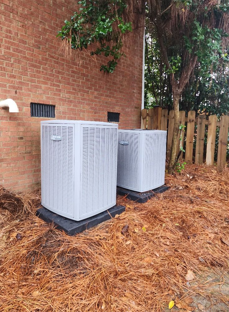 Two air conditioners are sitting outside of a brick building.