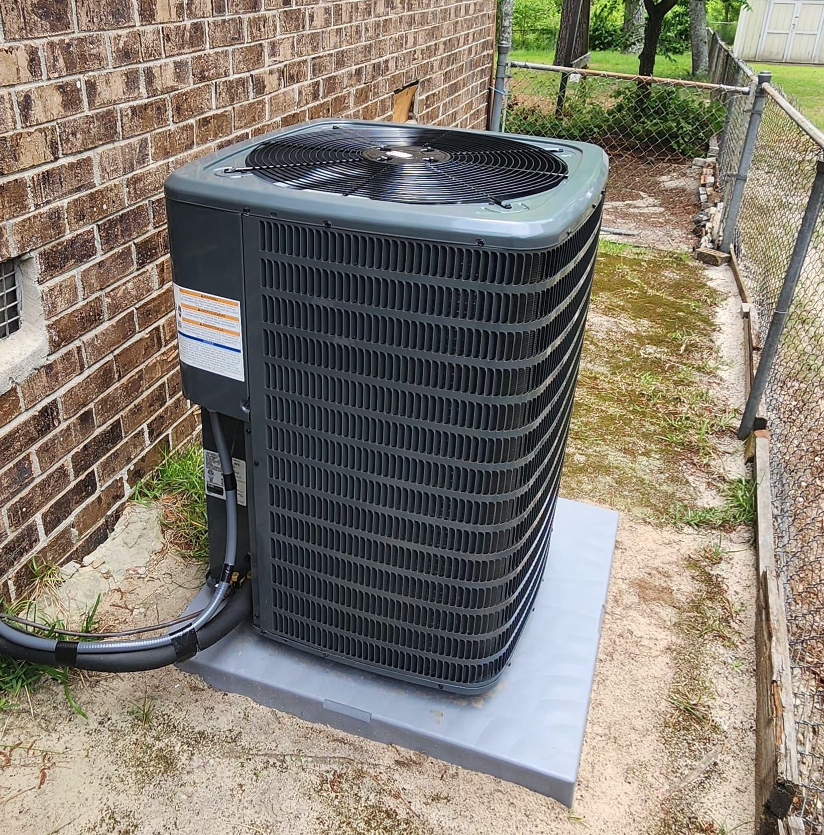 A large air conditioner is sitting outside of a brick building.