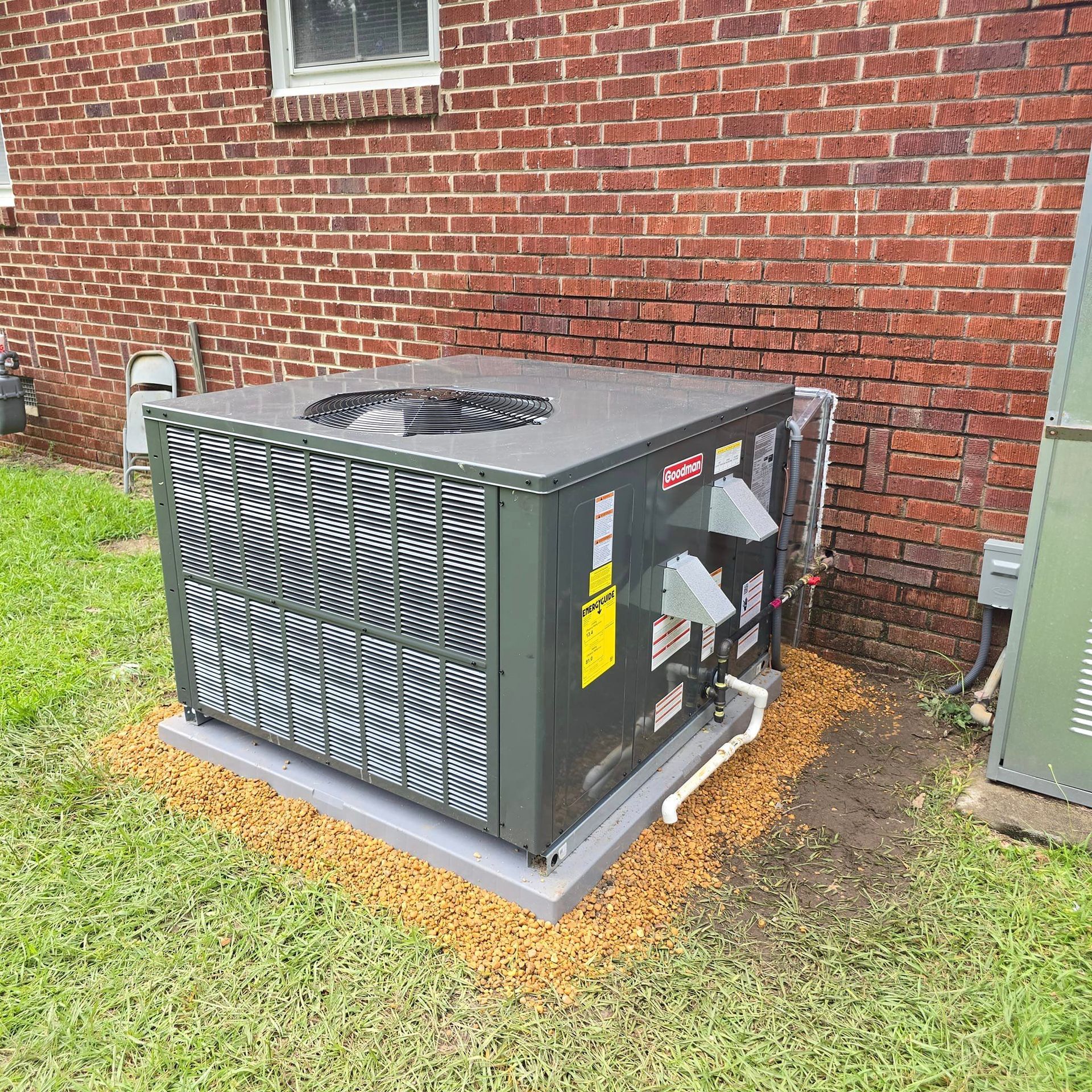 A large air conditioner is sitting in the grass in front of a brick building.