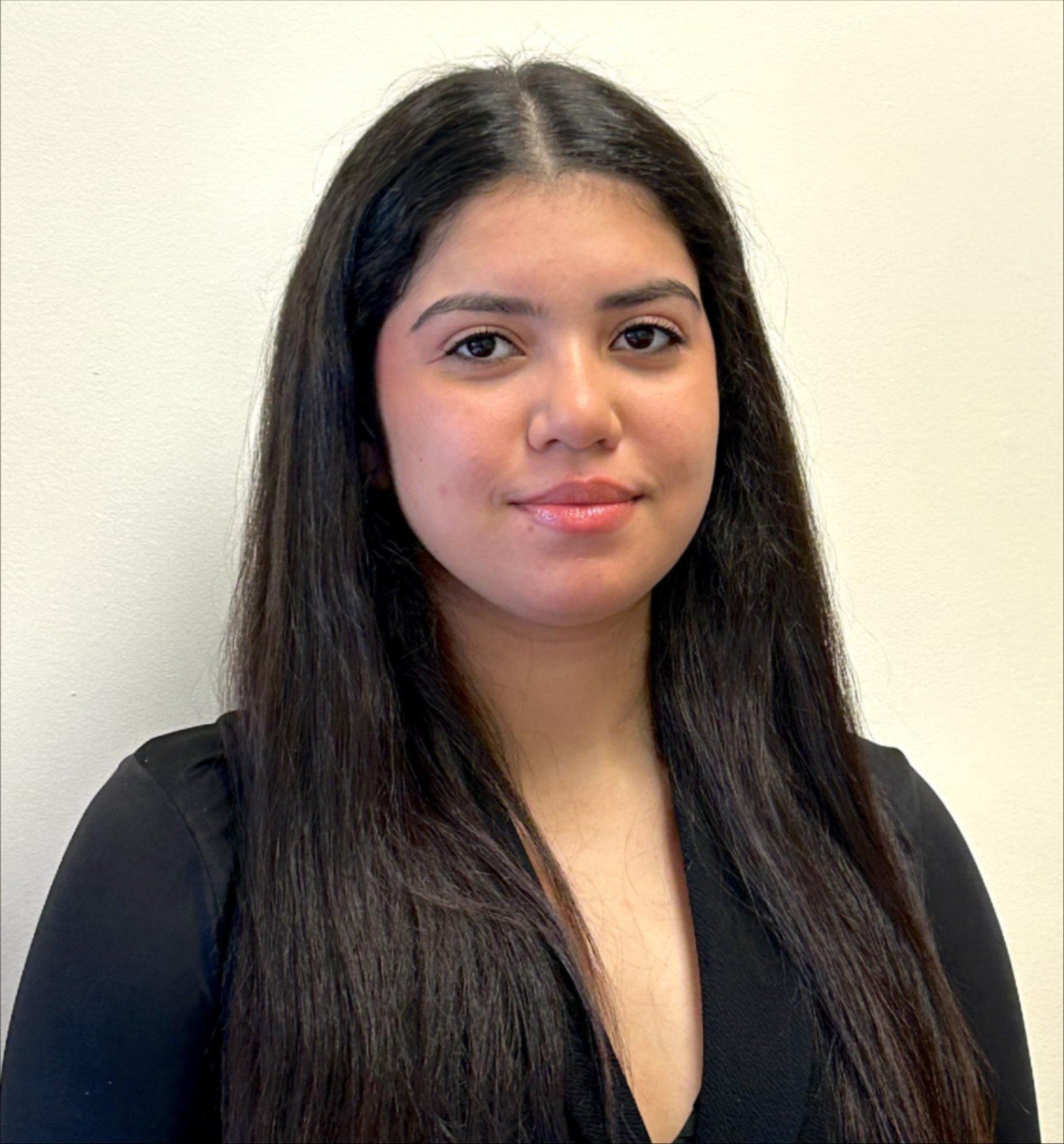 A woman with long hair is standing in front of a white wall.