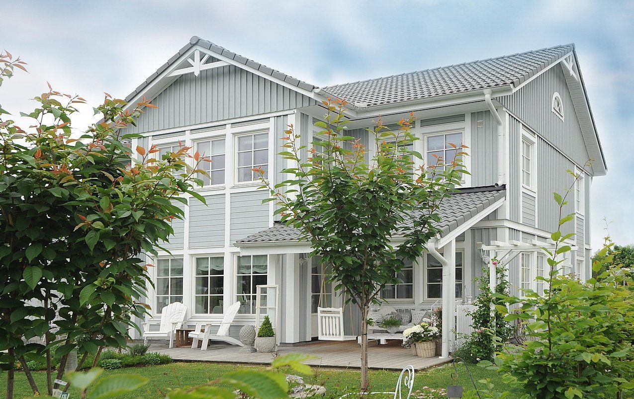 A large white house with a lot of windows is surrounded by trees and bushes.