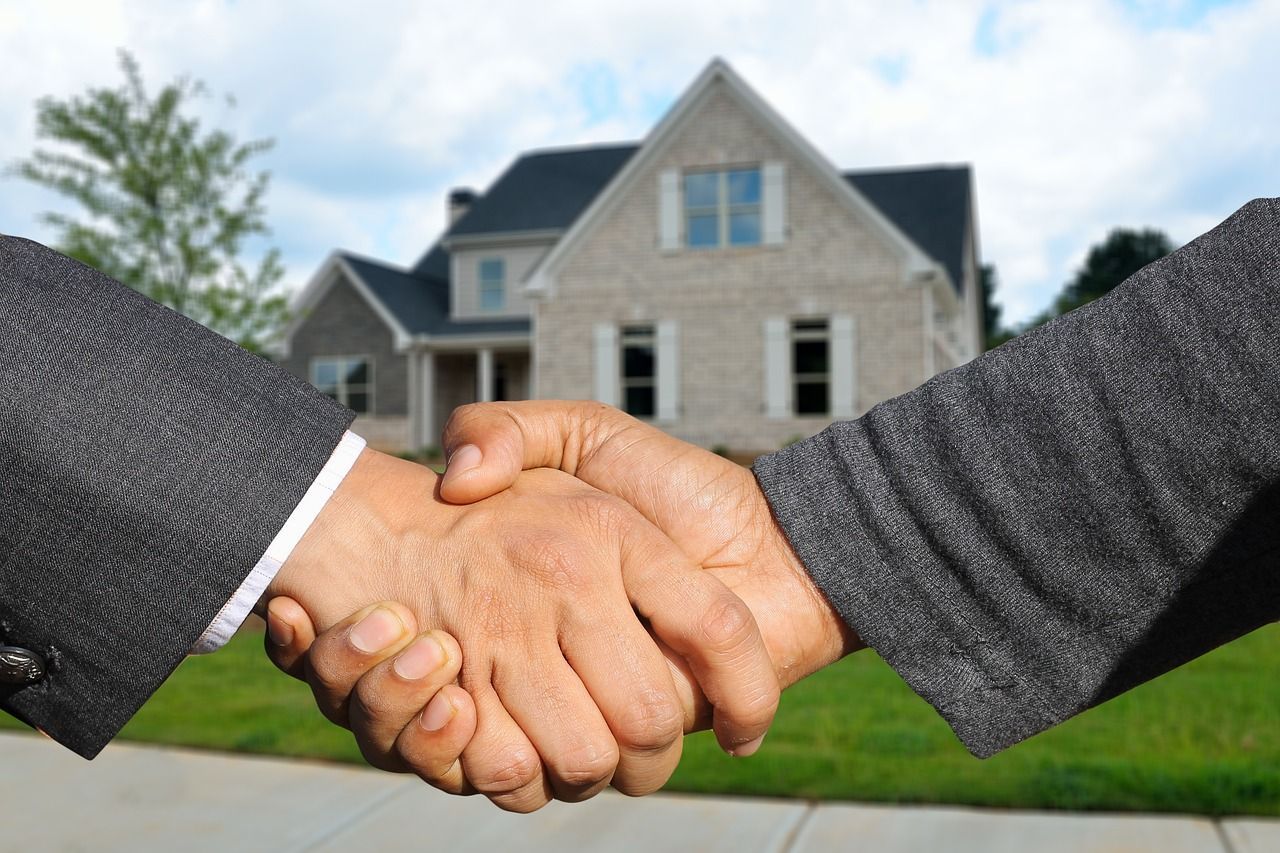 Two people are shaking hands in front of a house.