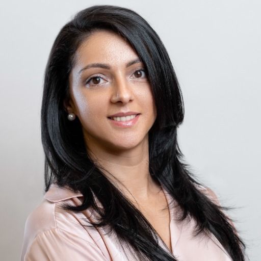 A woman with long black hair is wearing a pink shirt and pearl earrings.