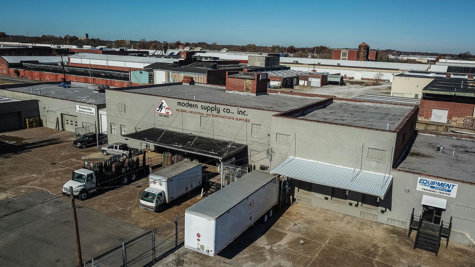 Aerial view of a warehouse building with loading docks, trucks, and surrounding urban landscape.