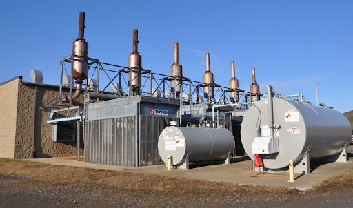 Industrial facility with metal tanks and smokestacks against a blue sky.