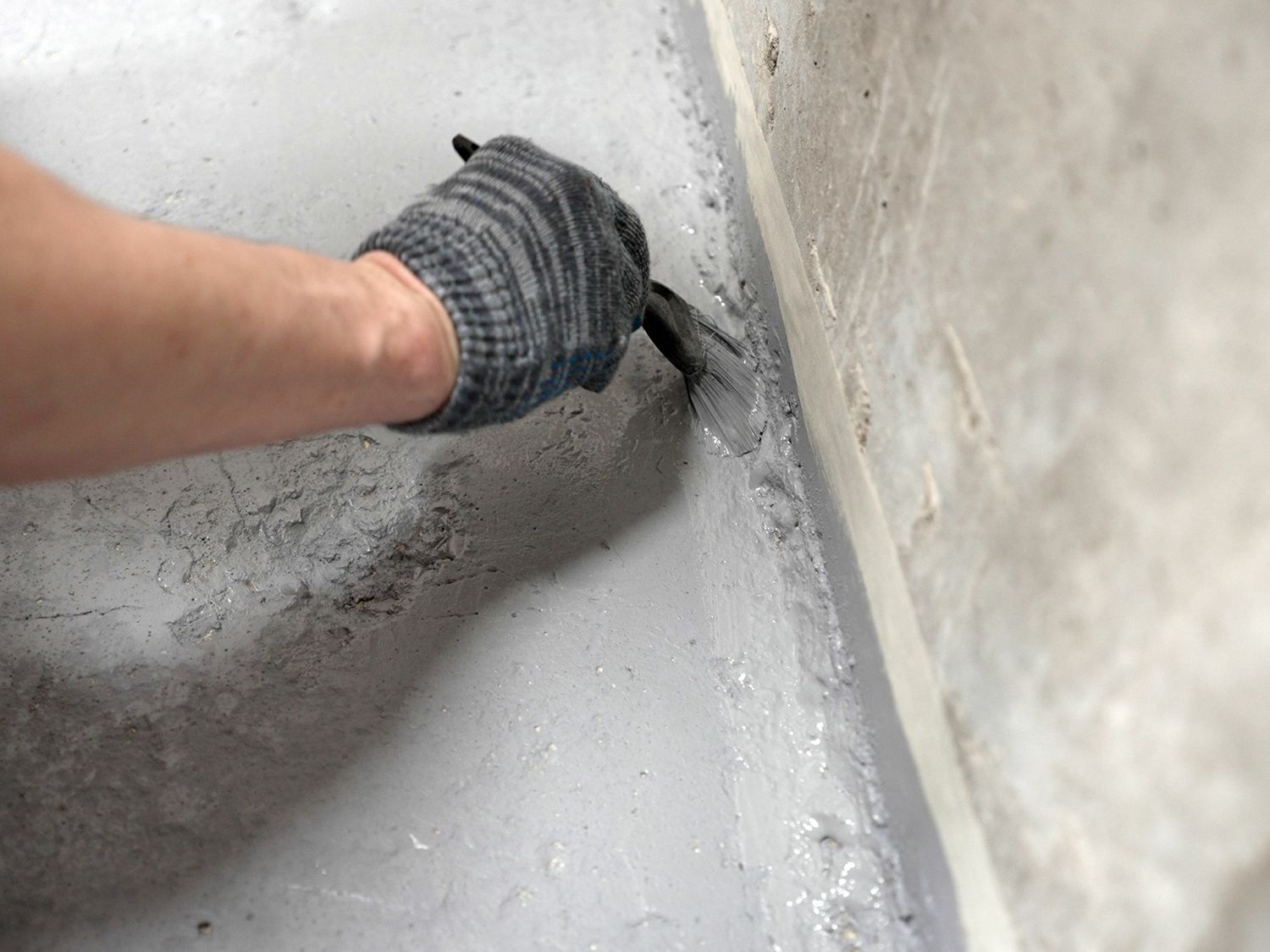 A person is painting a concrete floor with a brush.