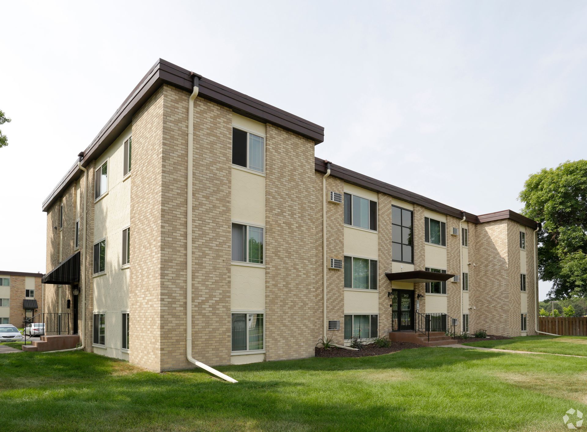 A large apartment building with a lot of windows is sitting on top of a lush green field.