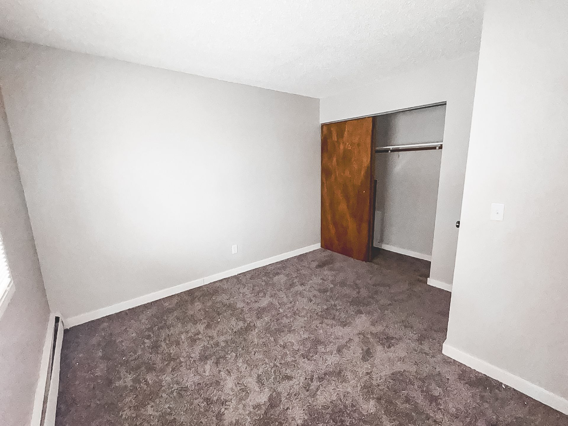 An empty bedroom with a closet and a window.