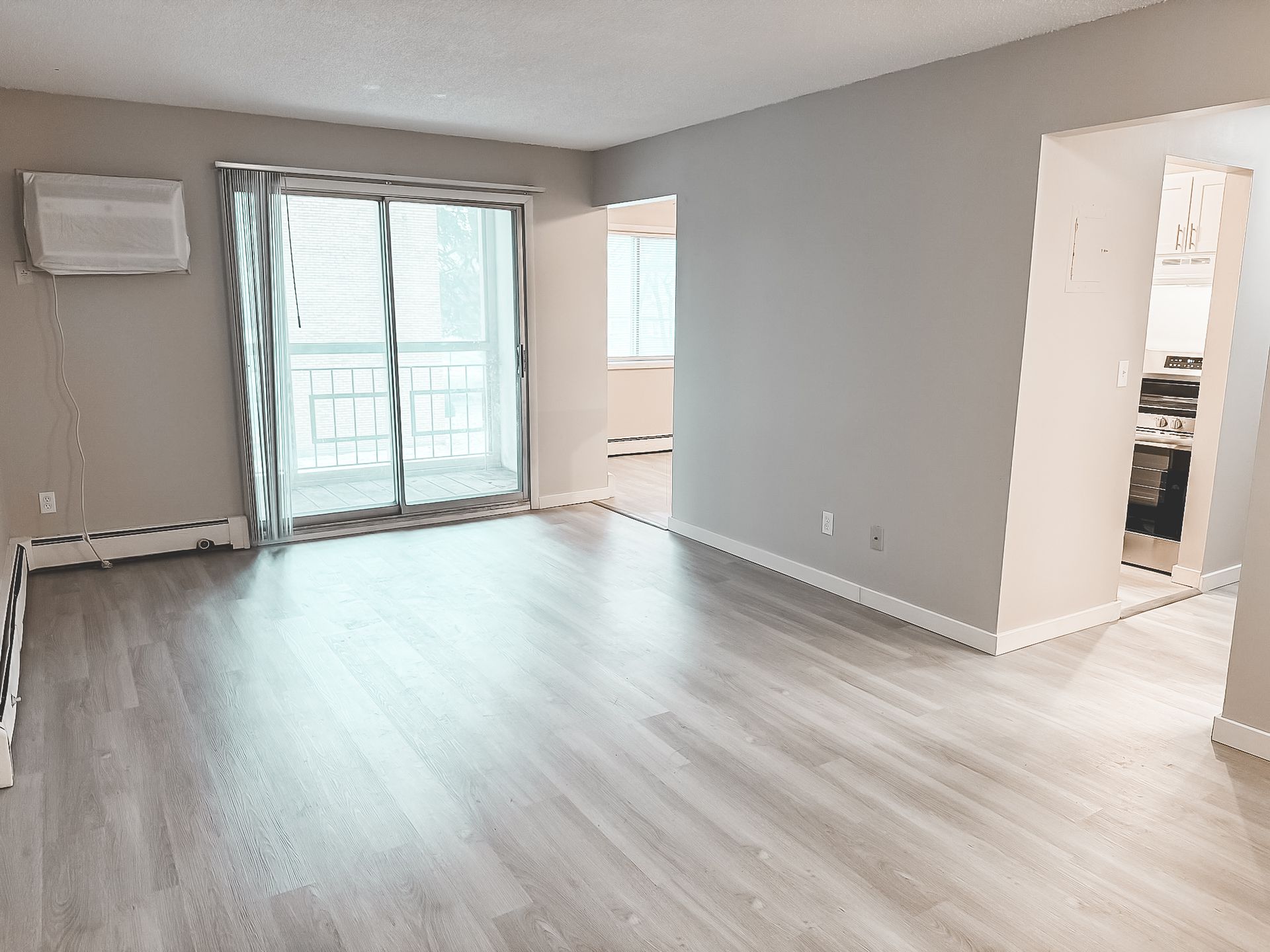 An empty living room with hardwood floors and sliding glass doors leading to a balcony.