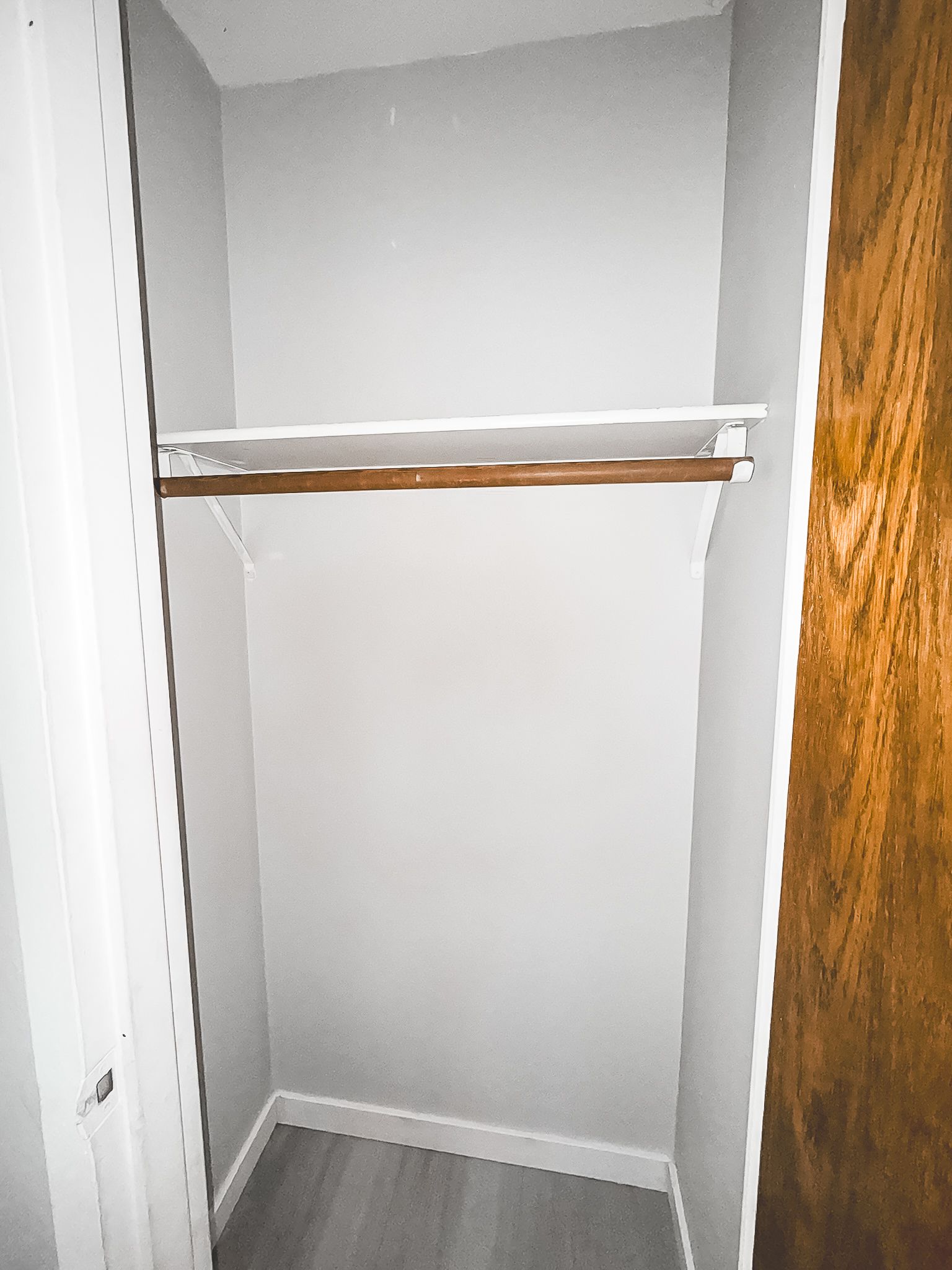 An empty closet with a wooden door and a wooden shelf.