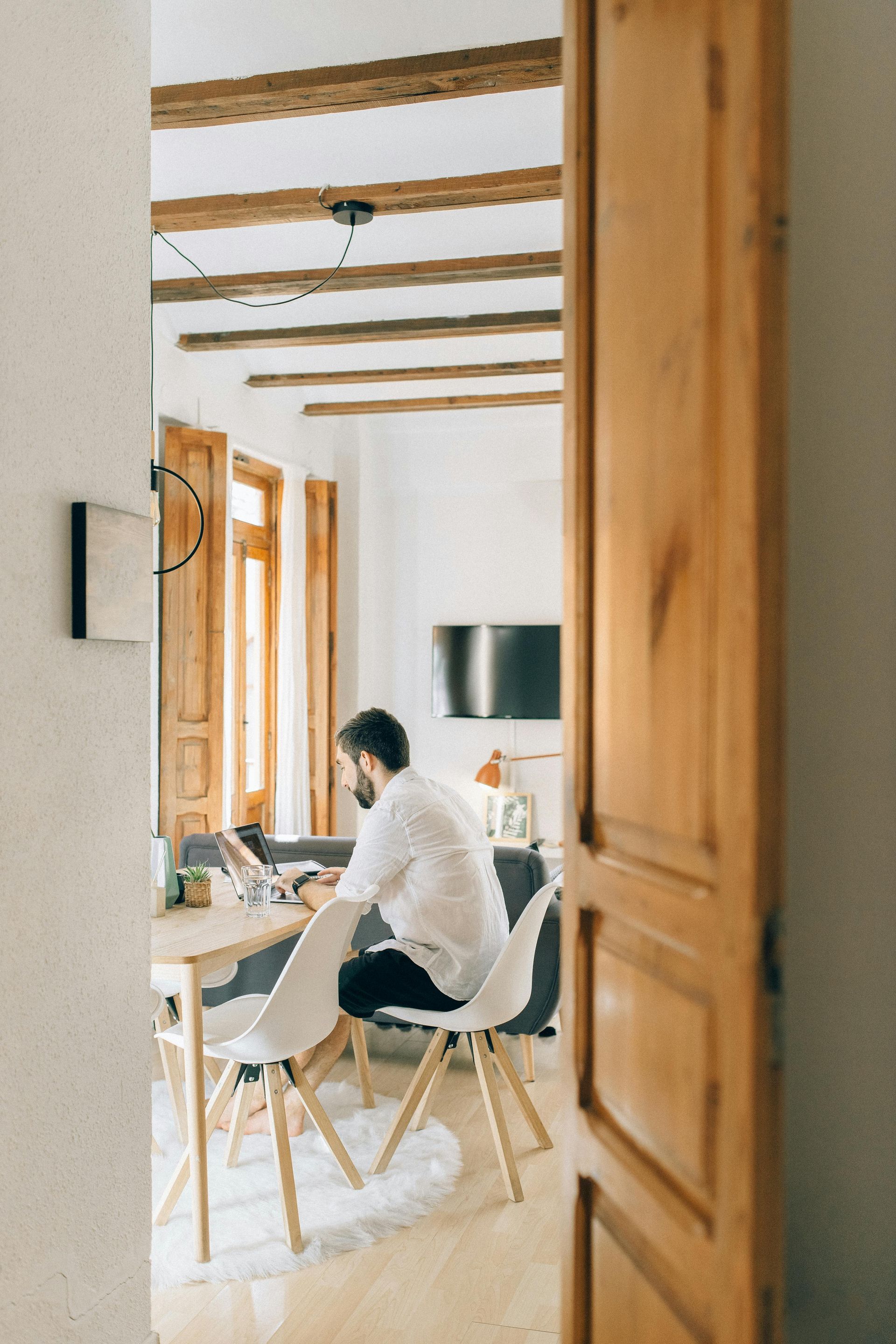 A man is sitting at a table in a living room using a laptop computer.