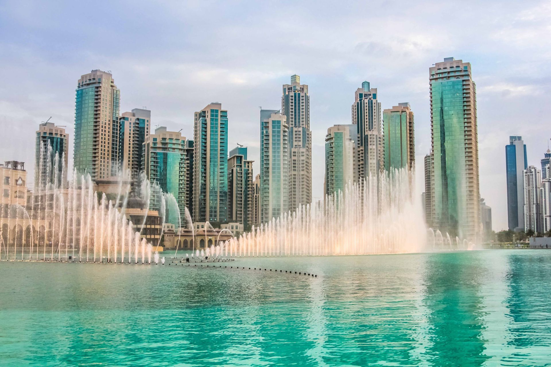 There is a fountain in the middle of the water in front of a city skyline.