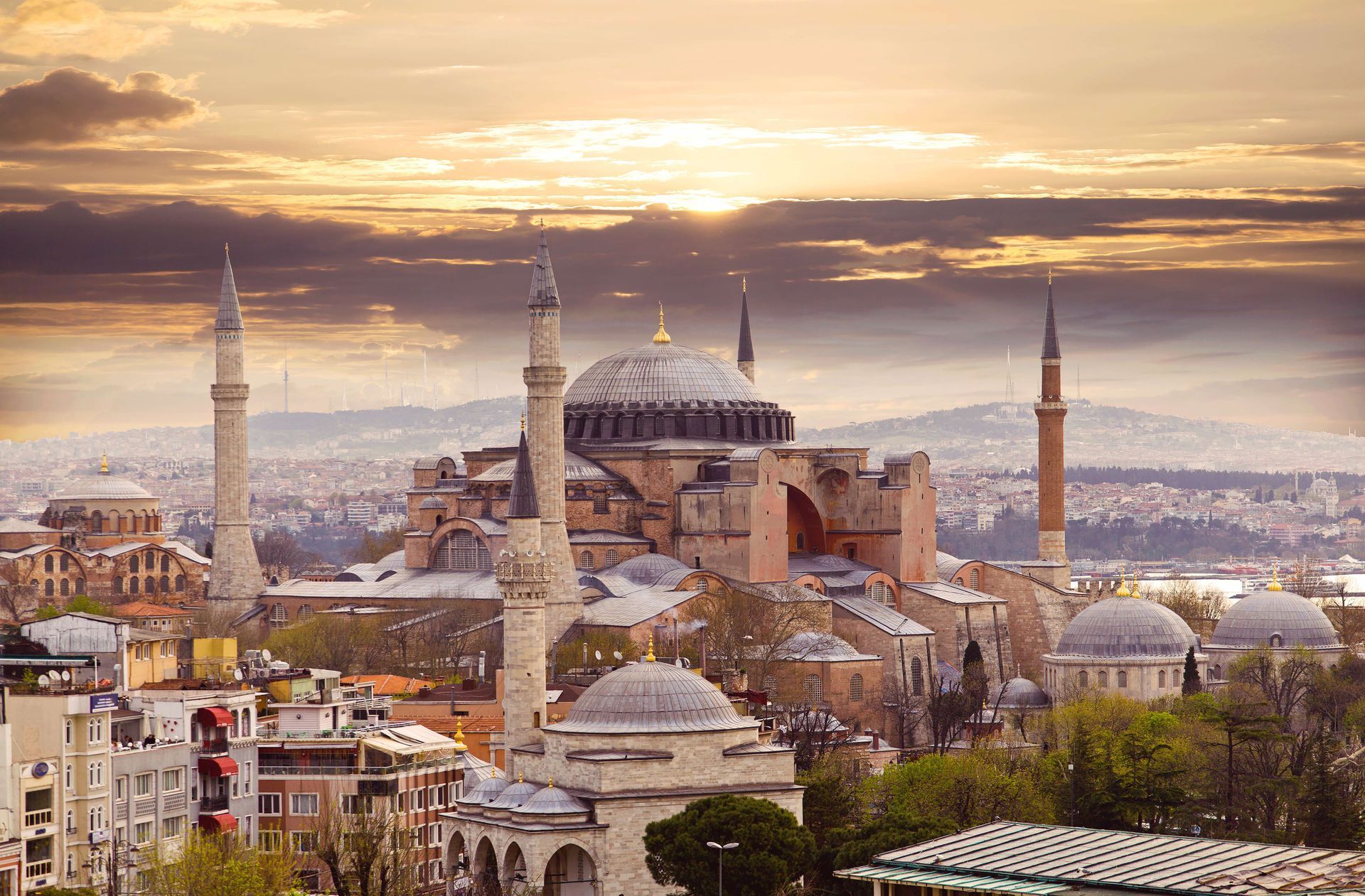 An aerial view of a city with a mosque in the foreground and a sunset in the background.