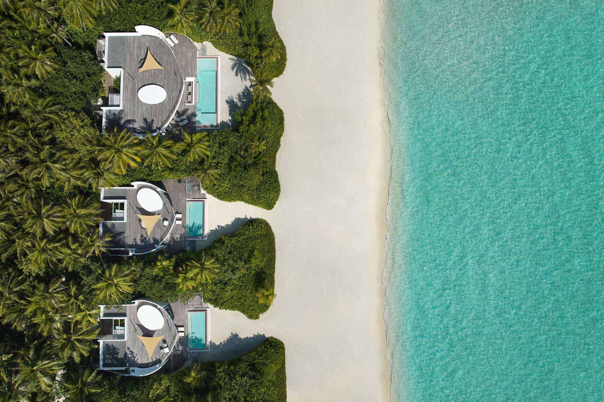 An aerial view of a row of houses on a beach next to the ocean.