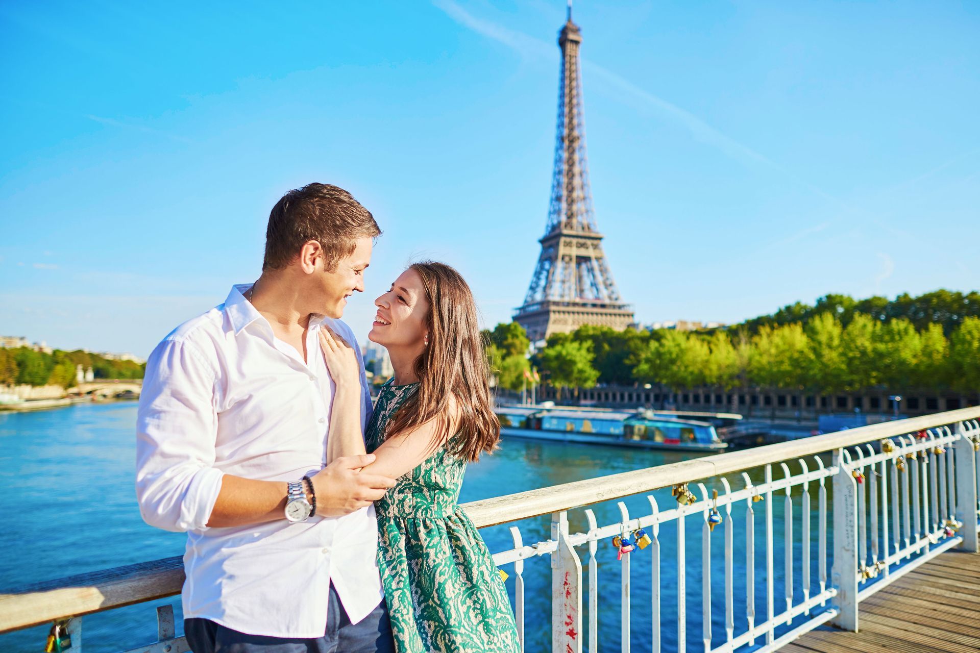 A man and a woman are standing on a bridge in front of the eiffel tower.