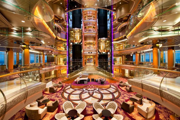 A large lobby on a cruise ship with a piano and chairs.