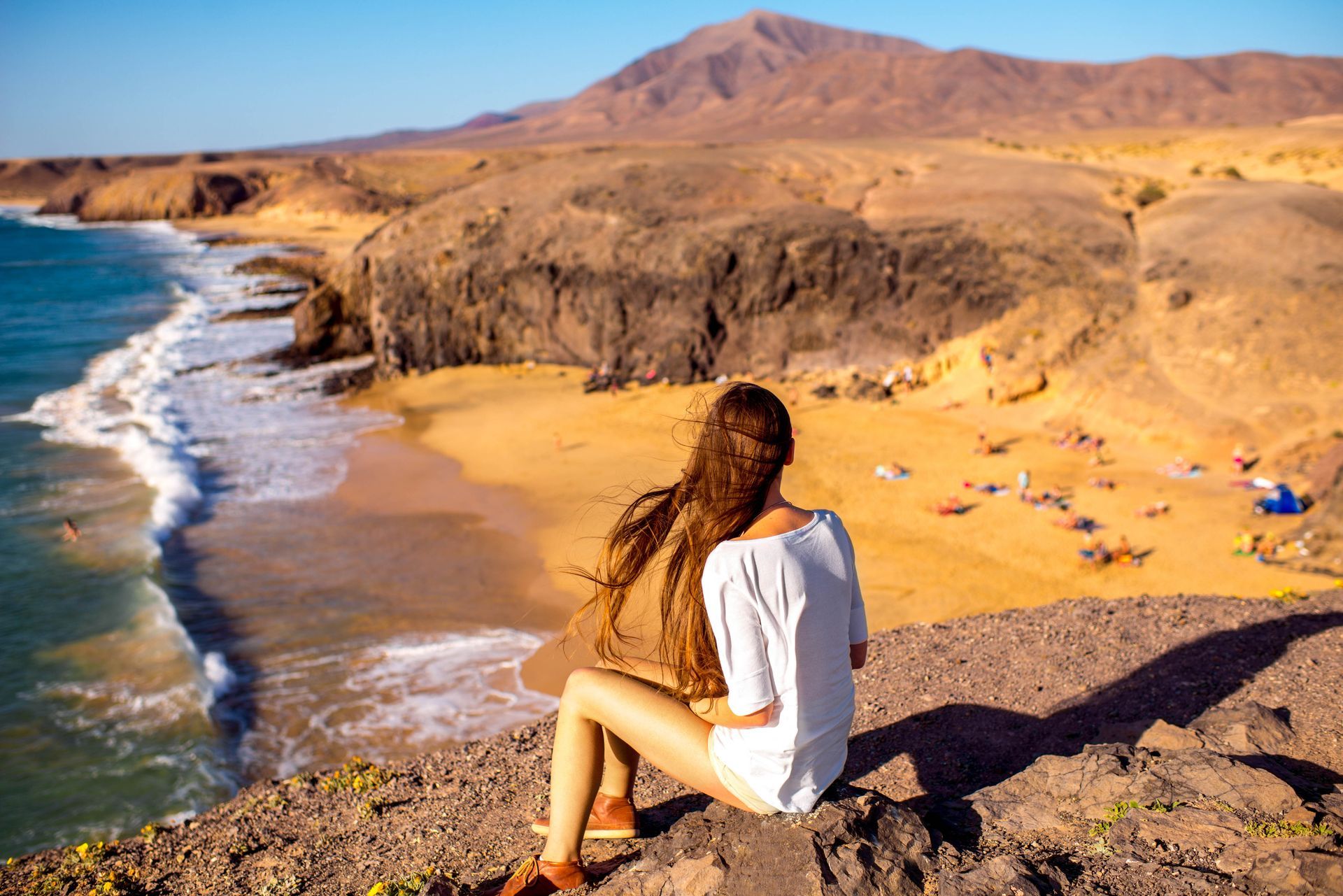 A young female tourist sitting and enjoying the beautiful view of Papagayo beach on Lanzarote island in Spain.