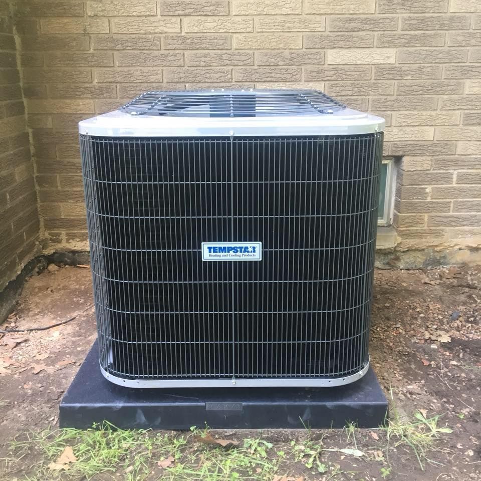 A black and silver Tempstar air conditioner unit sits outside a brick building.