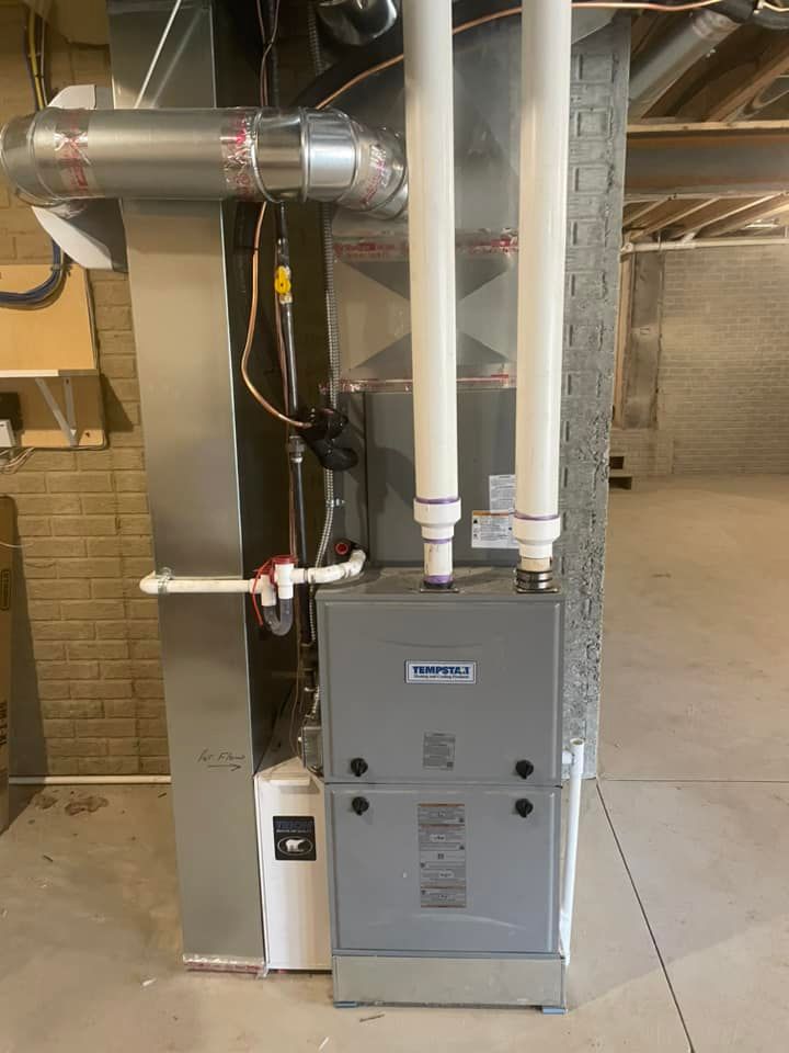 A furnace system in a basement. It has silver metal components, white PVC pipes, and a gray unit.
