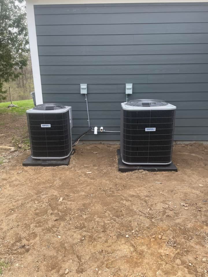 Two air conditioning units on concrete pads next to a gray building.