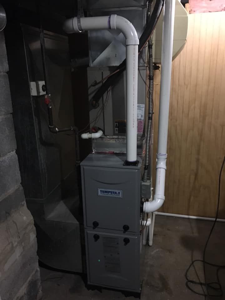 Furnace unit in a basement, with white vent pipes. Gray metal and wood surroundings.