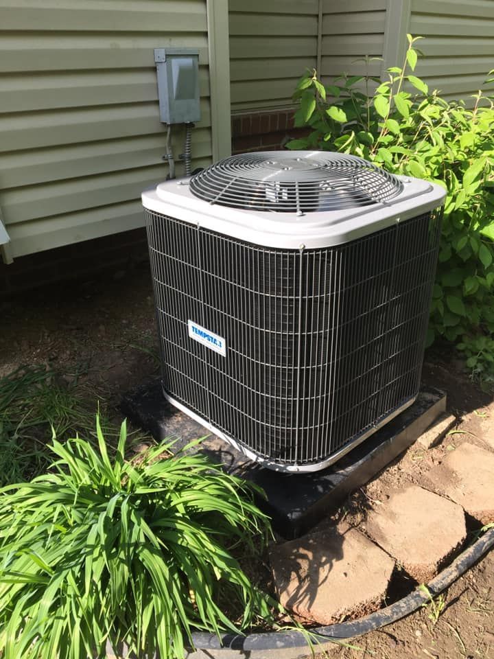 Air conditioning unit outside a house, with a protective metal cage and fan.