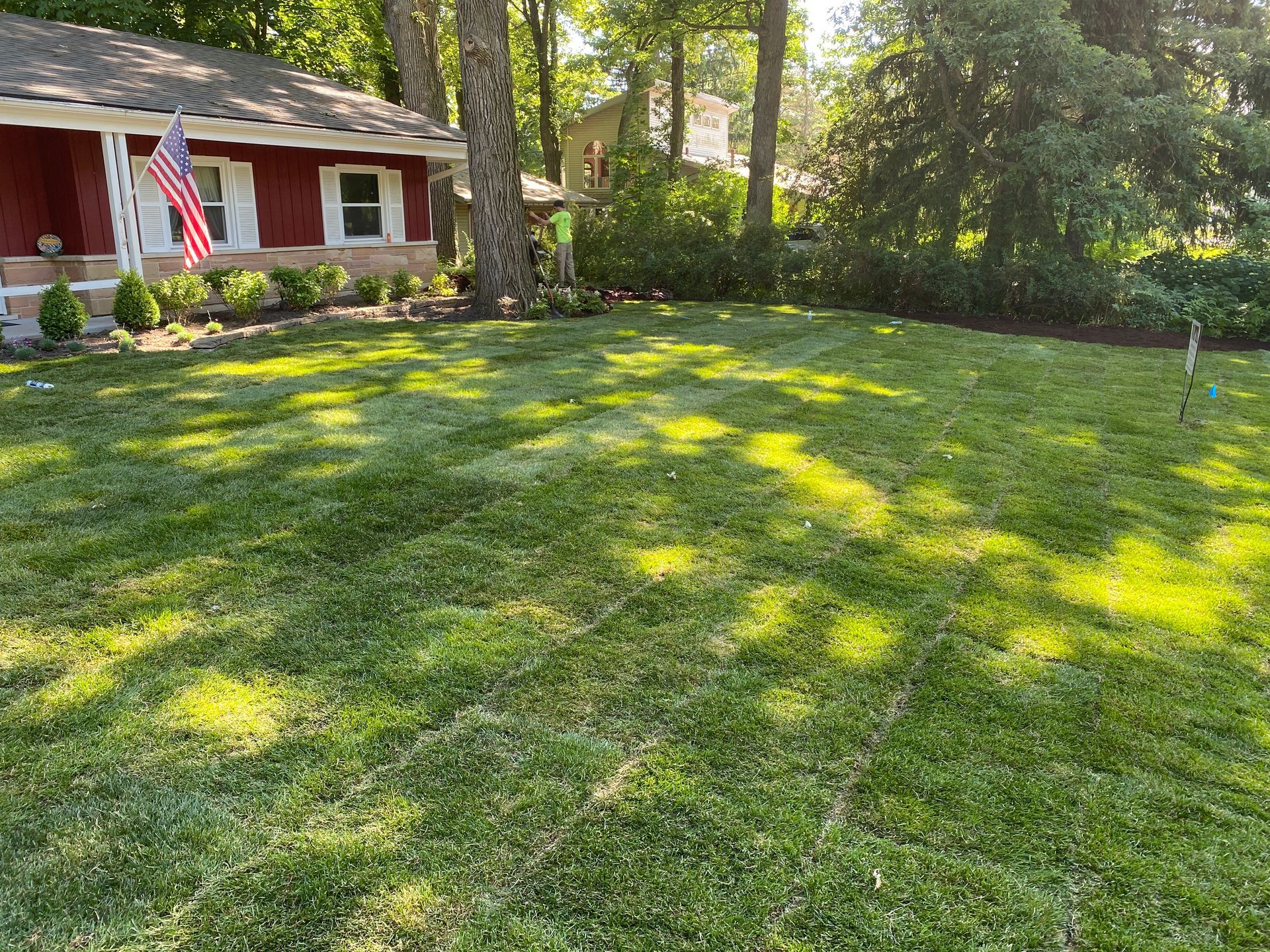 A lush green lawn in front of a red house with an american flag.